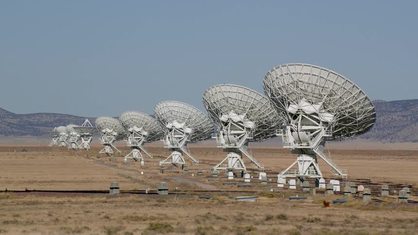 A landscape with satellite dishes with a mountain range the sky and clouds in the background