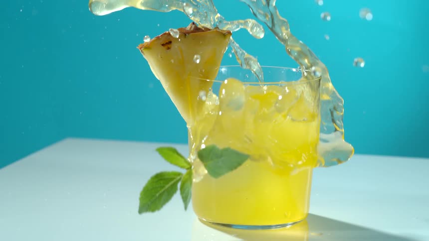 An ice cube being thrown into a glass with a drink in it