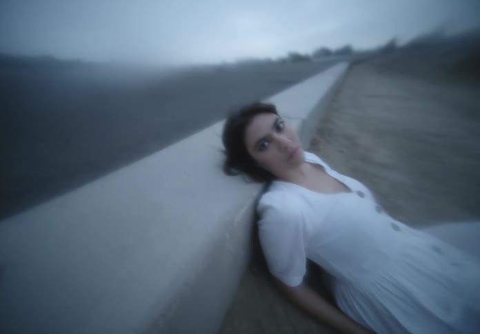 A woman in a white dress lying in the sand against a wall turns her head
