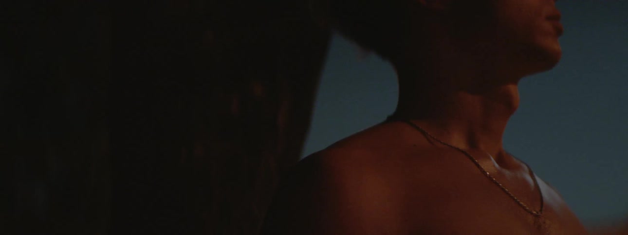 A man stands against an arched wall at night without a shirt on