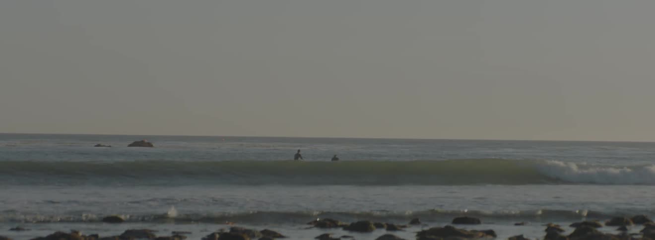 Two people are sitting on surfboards in the water just beyond the waves