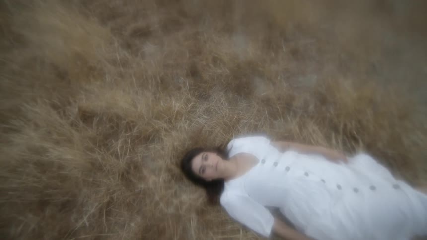 A woman in a white dress lies in a field of yellowing grass
