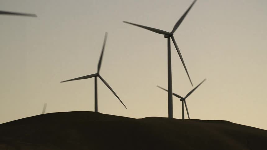 Wind turbines spin atop hills in the countryside on a cloudy day