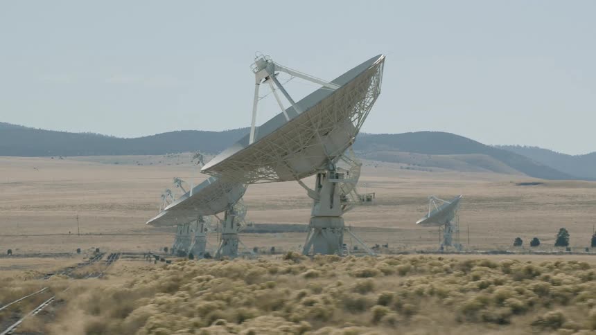 A landscape with train tracks and satellite dishes with a mountain range the sky and clouds in the background