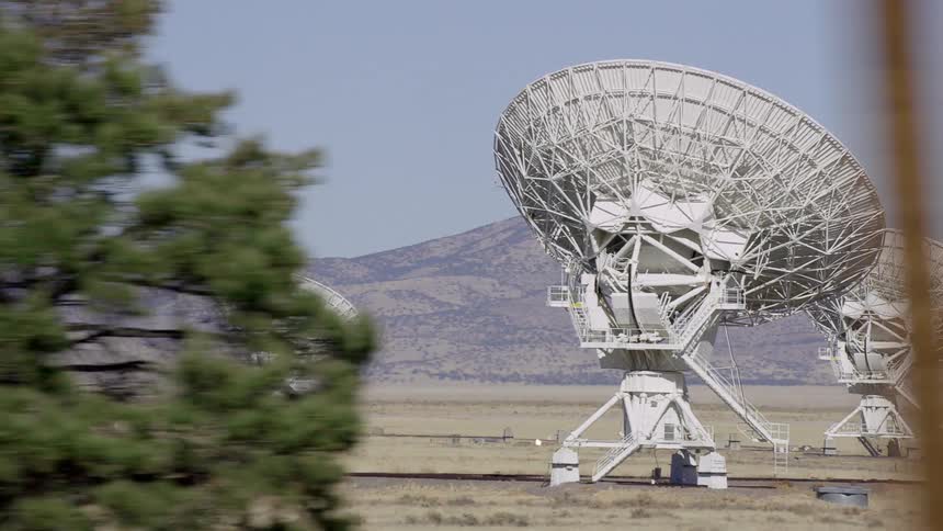 Large satellite dishes sit staggered in an open field near a canyon