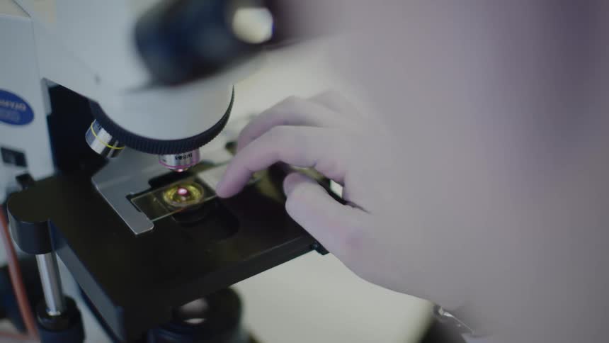 A scientist looking at a slide in a microscope in a lab