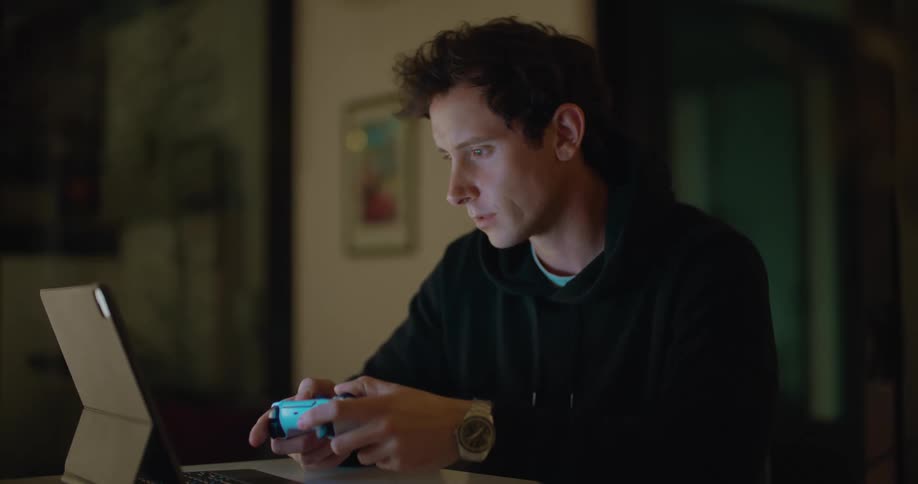 Young man sitting at the table playing video games on a laptop at home