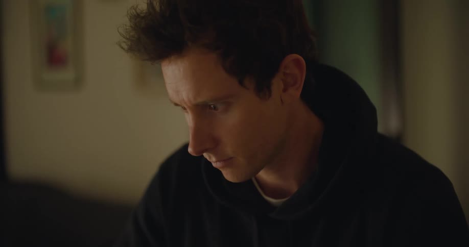 Man wearing hoodie plays game with game controller sitting next to computer
