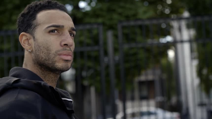 A man in a black jacket walks near a fence