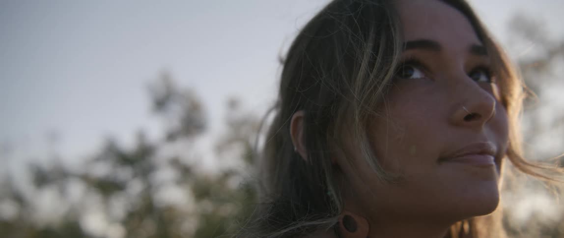 A woman with a nose ring with trees the sky and clouds in the background
