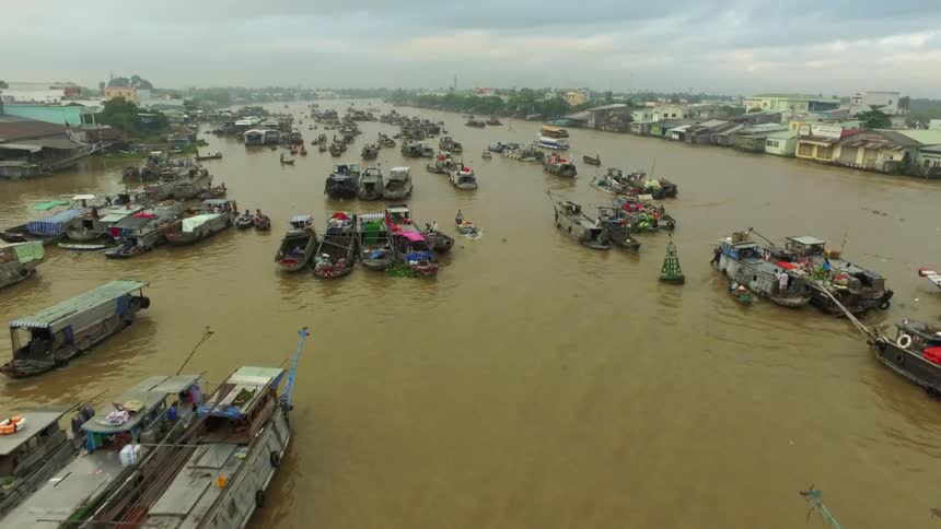 Aerial view of several group of boats and barges over the brown waters of a river through a small city