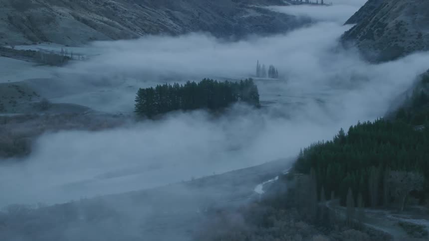 A mountain valley shrouded in fog during the day