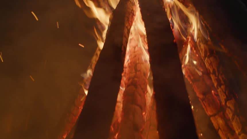 A fire burns atop a number of pieces of woods that are stacked together