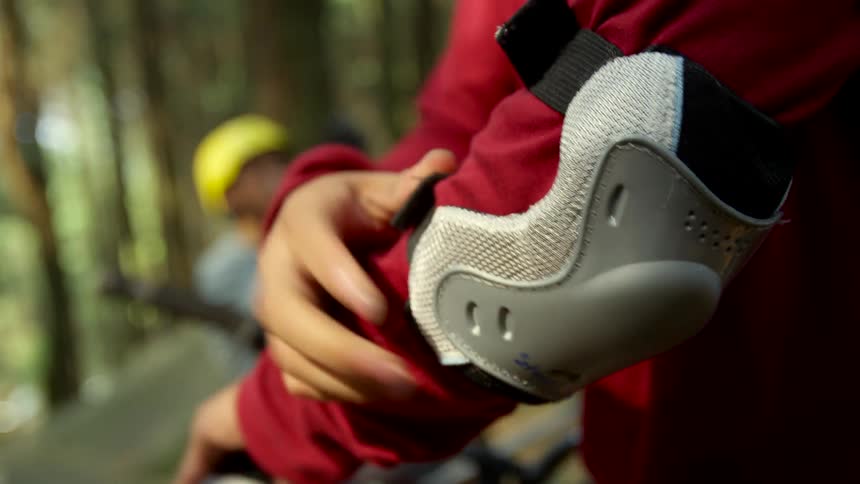 Teenager adjusting an elbow pad before riding bicycles on the forest with friends