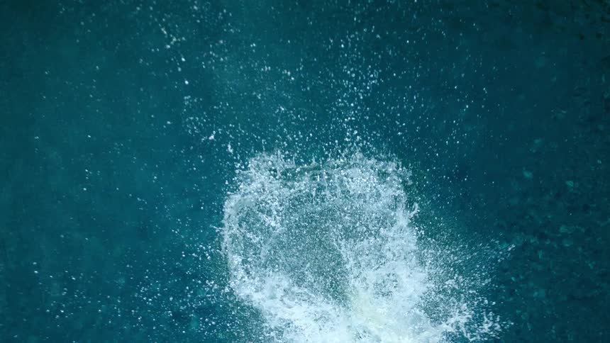 An aerial view of a rock falling in to the water and splashing