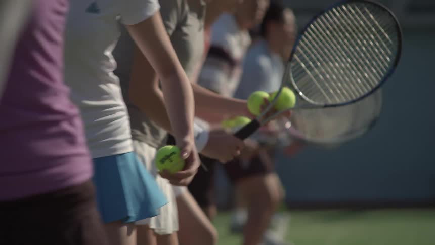 A line of people with tennis rackets on a court practice serving