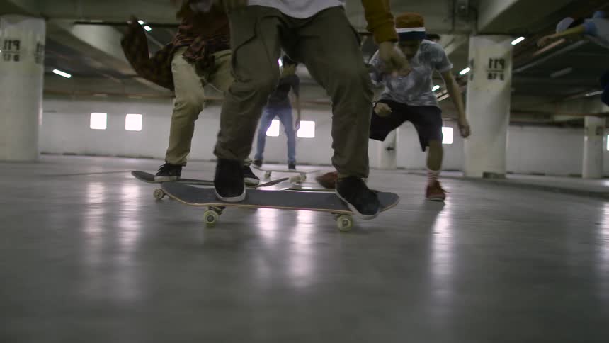 Group of teenagers ride skateboards inside a parking garage doing tricks