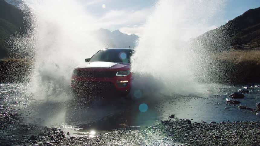 Suv splashes through stream bed in valley bordered by mountains