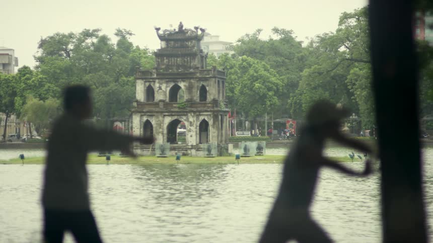 Silhouette of two men parcticing tai chi in front of a monument in the middle of a lake