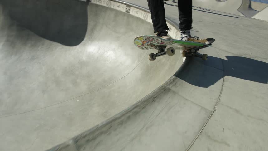 A skateboarder grinds across the top of a skate bowl before skating inside