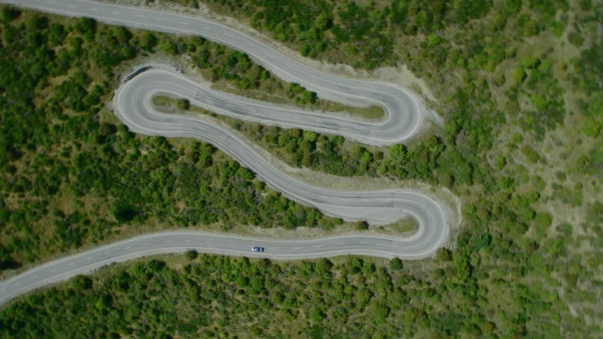 Aerial view of a blue car driving down the twisting mountain road
