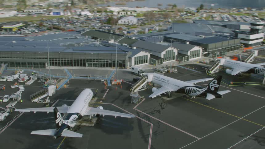 An airport with buildings and airplanes with a lake and a mountain range in the background