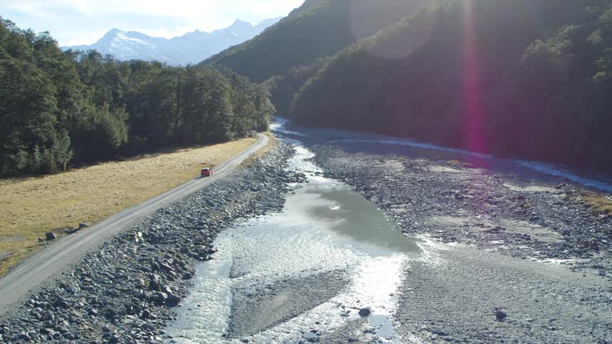 Aerial view of a red van driving on a road near a river through the mountains at morning