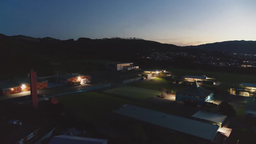 Silhouette of hill ridge with trees overlooking homes with glowing lights