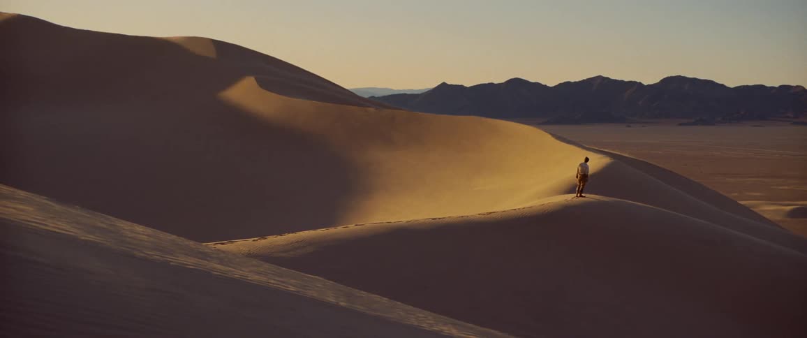 Mountains on the horizon back a person standing on top of a sand dune before starting to walk
