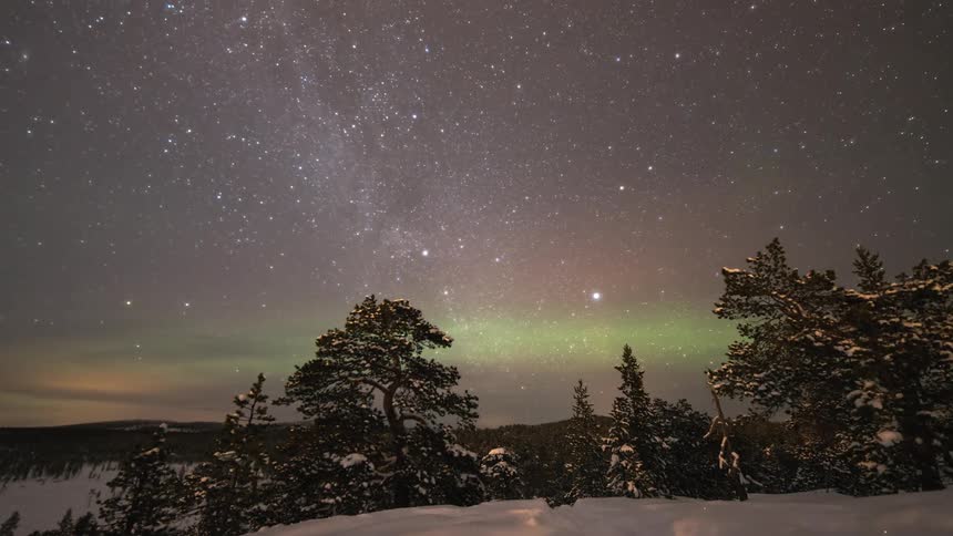 The Milky Way turning with northern lights in the distance