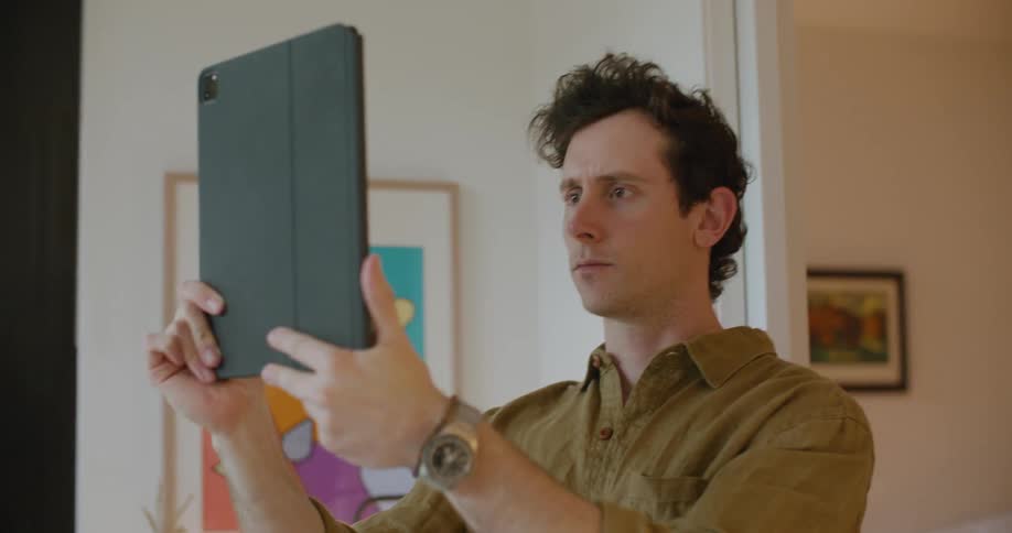 A man holds his table computer up high as he uses its camera while indoors