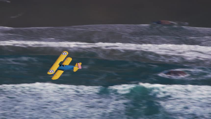 An airplane flying over a coast with waves of water with cliffs in the background