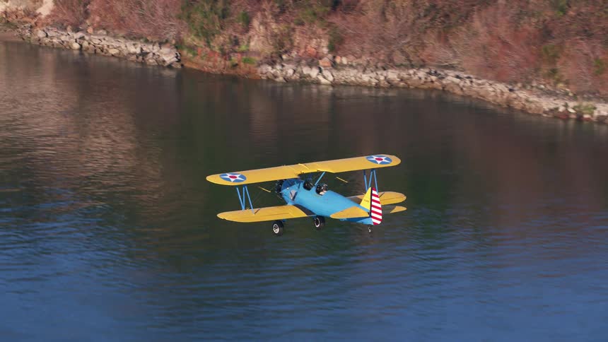 Pilot flies a blue biplane over the ocean water