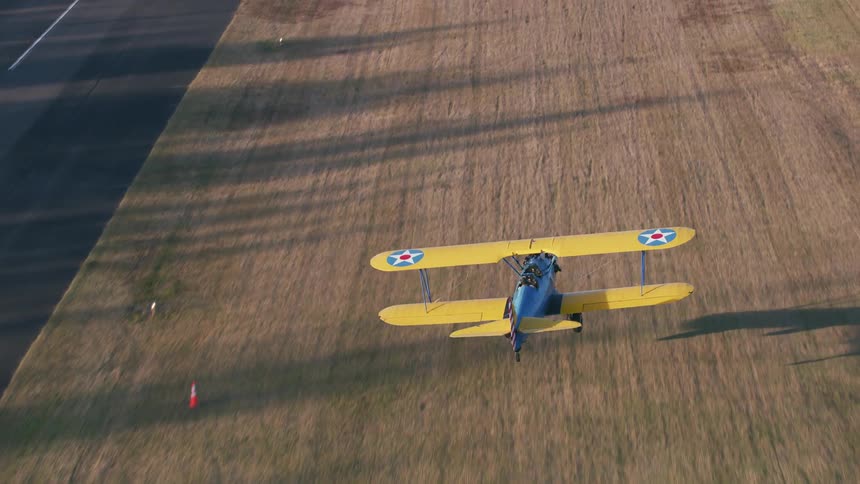 Yellow biplane lands in field next to runway