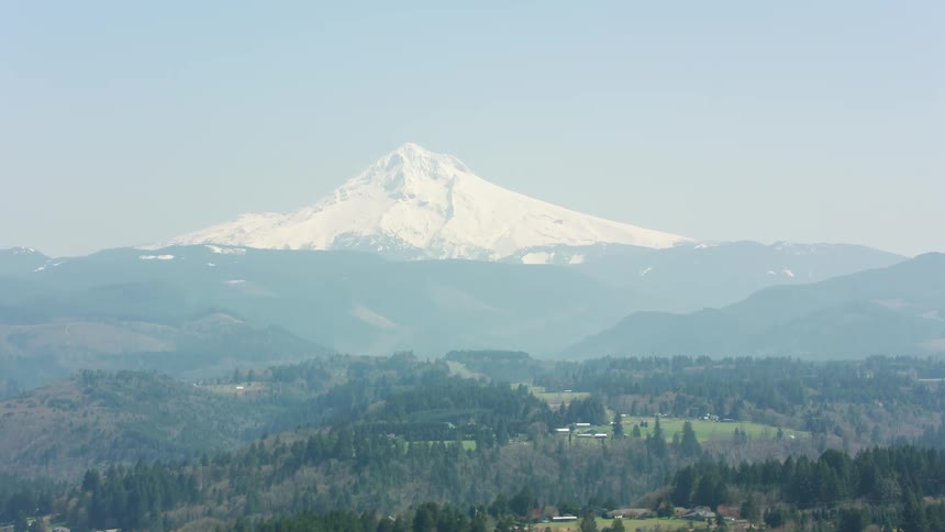 A landscape with hills and trees with a mountain range the sky and clouds in the background