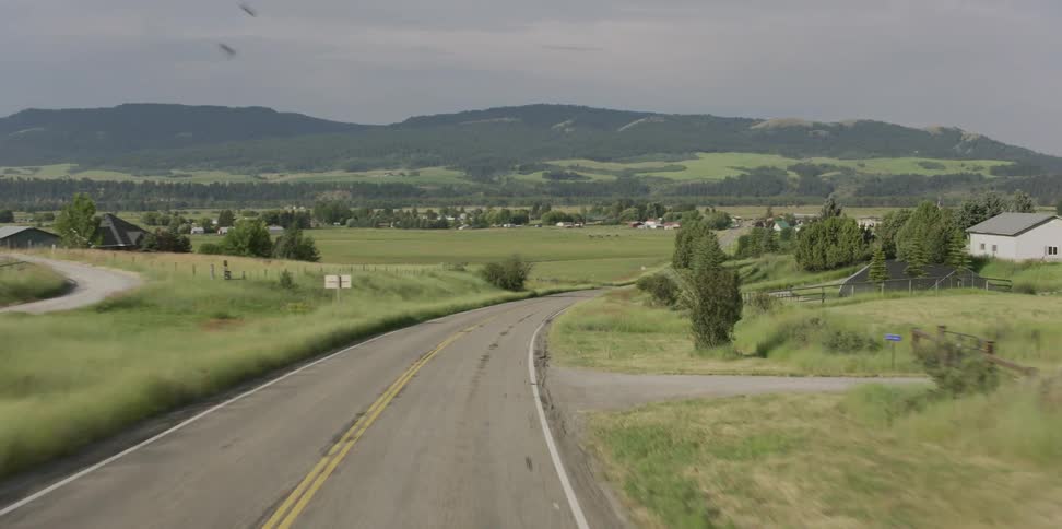 Vehicle drives on country road next to green hill in the countryside