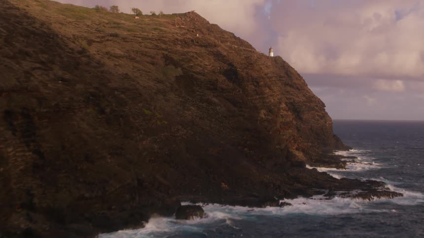 Waves break and splash against the rocks with a lighthouse on a cliff