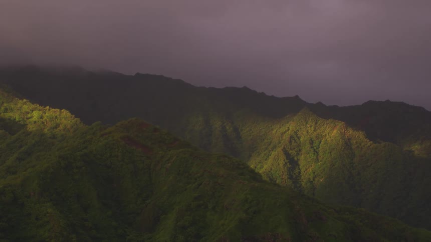 Green covered mountain ridge and mountains on the horizon under a dark cloudy sky