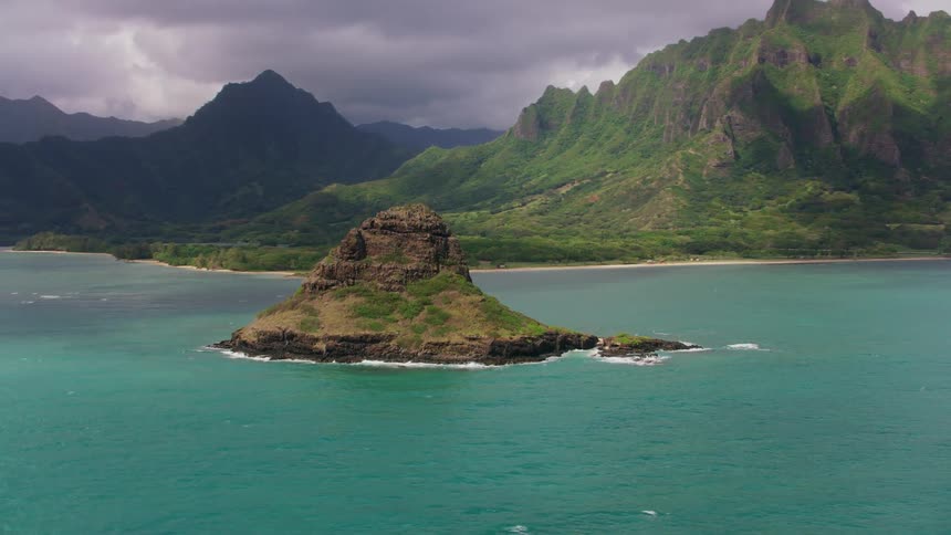 Ocean waves splash against the rock of a small island near coastal cliffs and ridges