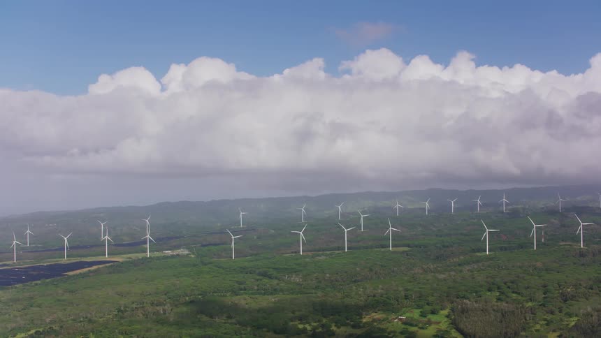 Fog covers mountains and row of wind turbines nearest to horizon as turbine blades slowly rotate