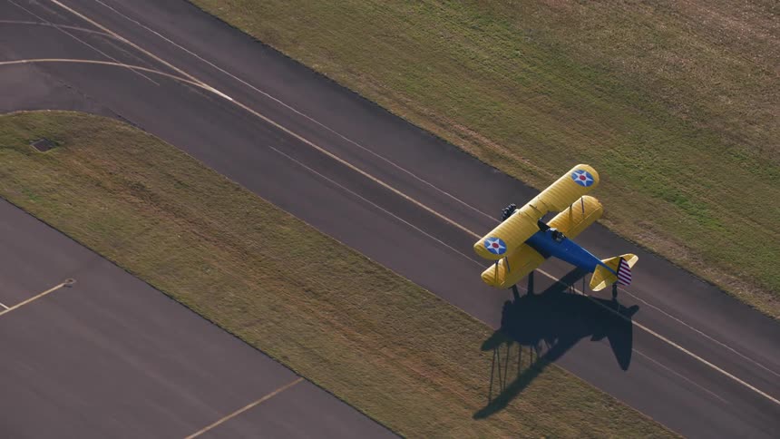 A yellow and blue vintage style airplane takes off from an airstrip