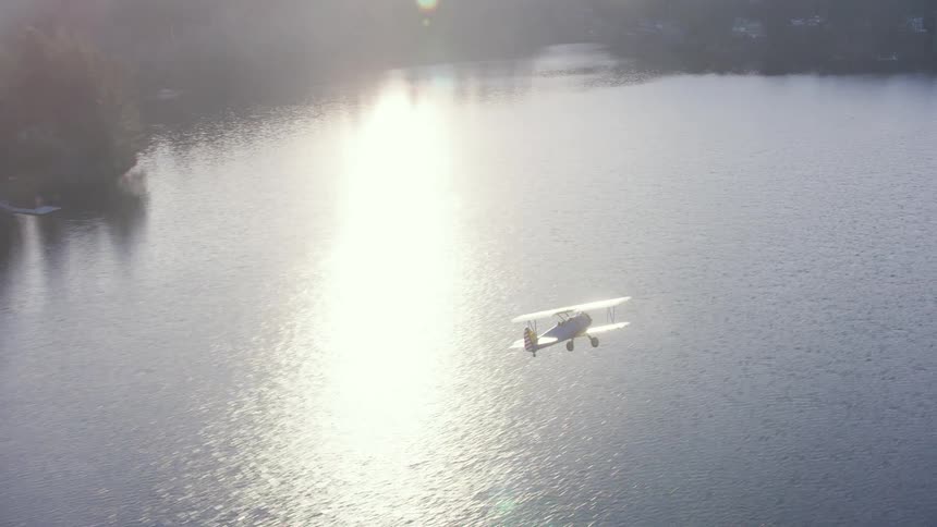 An airplane flies over a rural tree surrounded lake