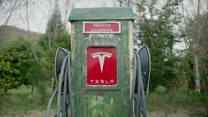 A tesla charging station is by the trees