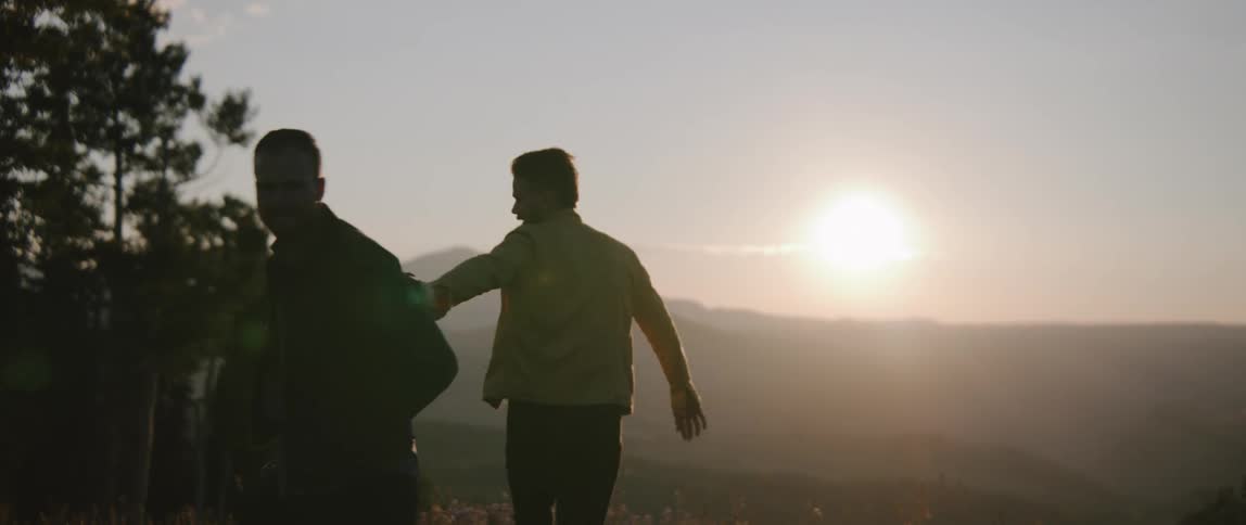 Two men holding hands and playing around at sunset
