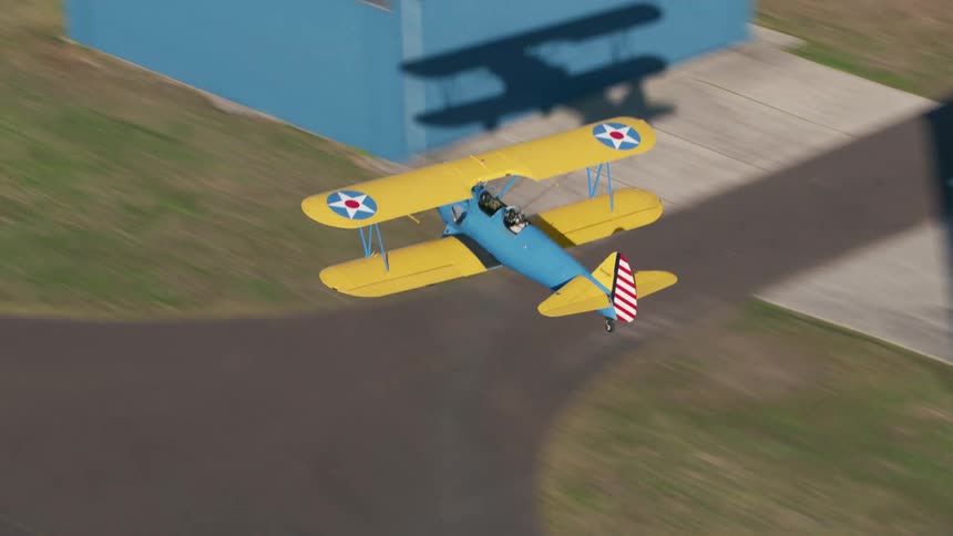A colorful by plane flies at low altitude above a runway before quickly getting altitude