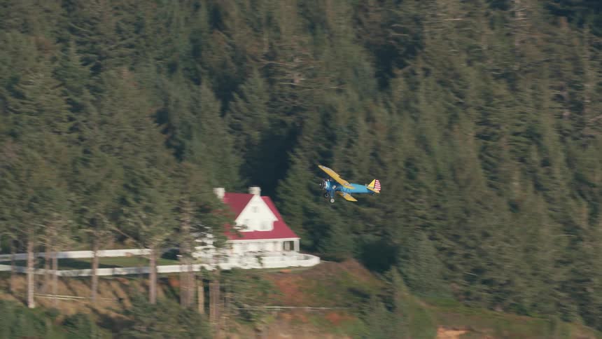 A plane flies over a rocky coastal area filled with caves and remote houses