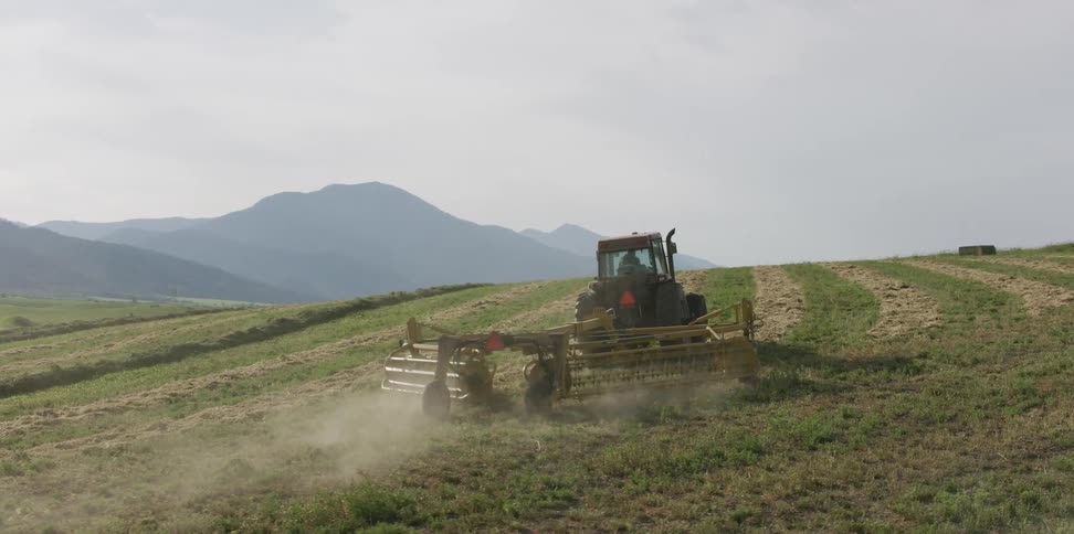 Tractor pulling agricultural machinery over the crops on a field at morning