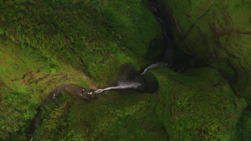 Aerial view of a waterfall dropping into a deep ravine between green hills
