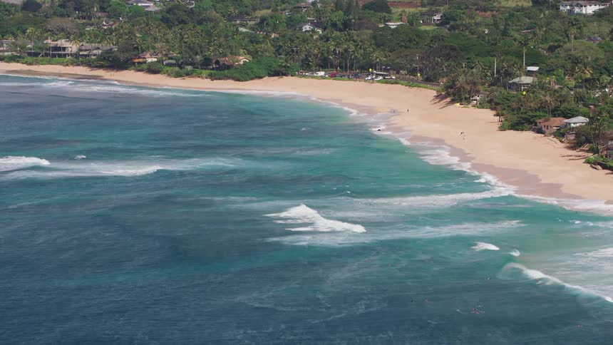 Aerial view of the blue ocean waves gently crashing on a beach next to a coastal town
