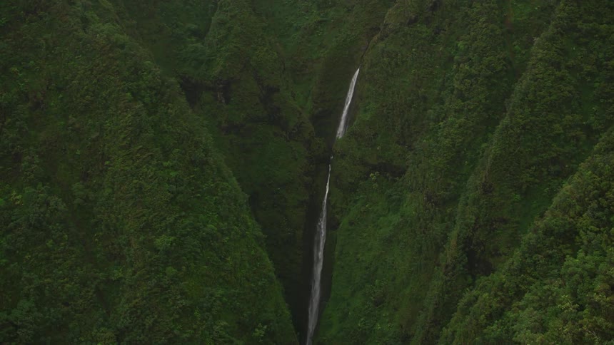 White foaming waterfall flows down steep forest covered mountain into narrow valley